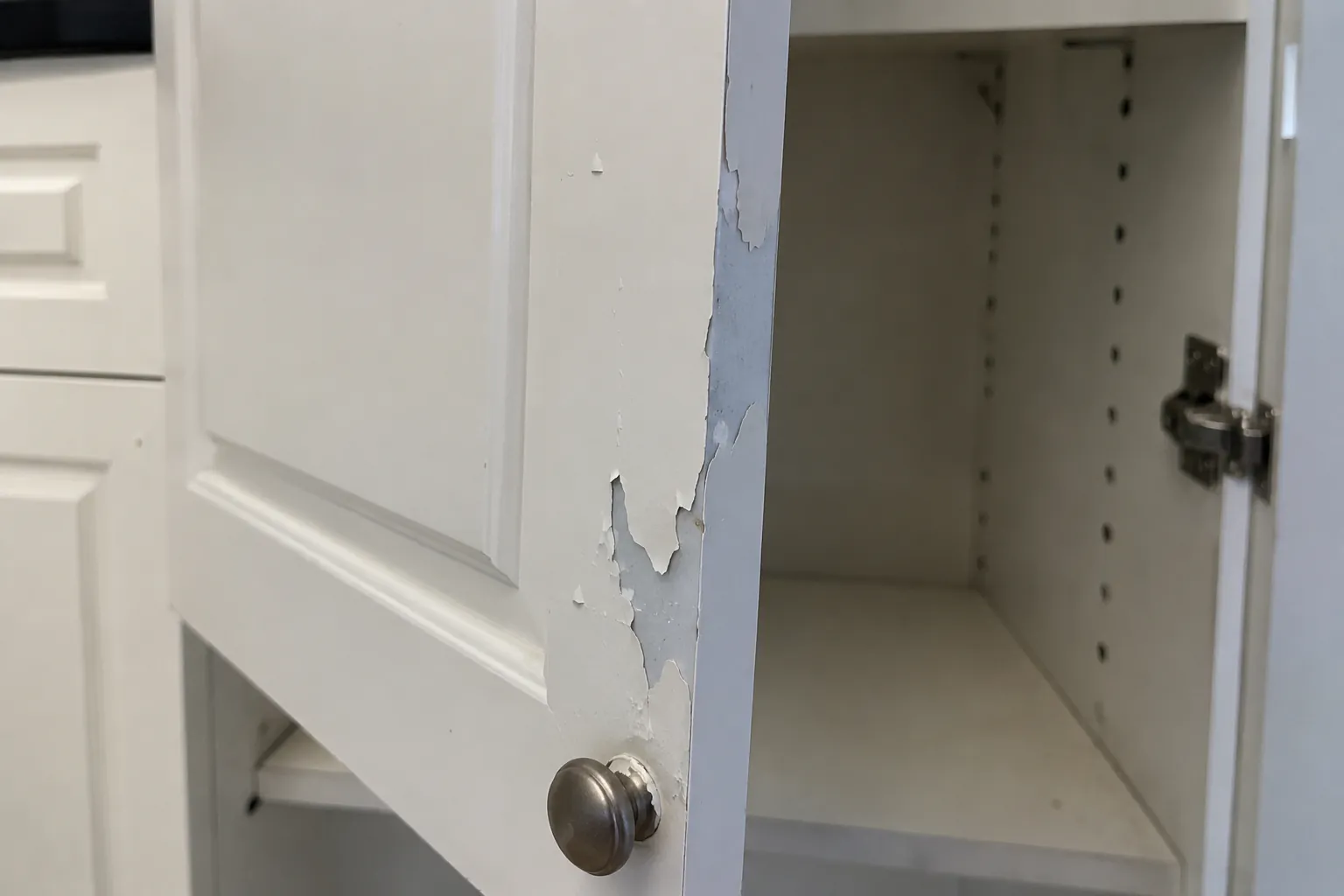 Maling som flasser av en kjøkkenfront ved håndtaket og viser det glatte underlaget under