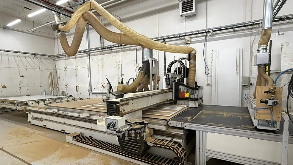 CNC-maskin som freser ut fronter, med avsugsslanger over maskinen